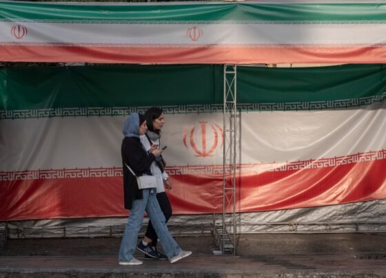 Two young Iranian women walk past the country's flags in northern Tehran, Iran, on June 30, 2025, following the ceasefire between Iran and Israel.