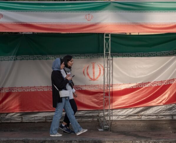 Two young Iranian women walk past the country's flags in northern Tehran, Iran, on June 30, 2025, following the ceasefire between Iran and Israel.