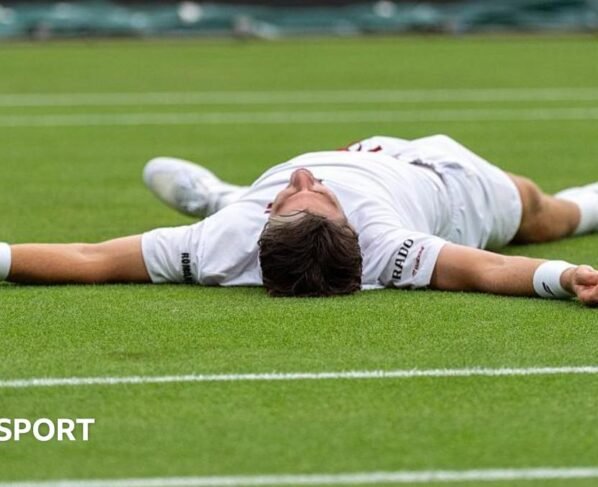 Cameron Norrie celebrates by falling on to the court